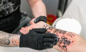 Ręce w czarnych rękawiczkach smarują świeży tatuaż na przedramieniu. To kluczowy etap pielęgnacji, by wiedzieć, czym smarować tatuaż.