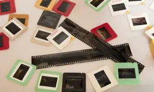Stare klisze filmowe i slajdy, niektóre w kolorowych ramkach. Widać fragmenty negatywów z perforacją.