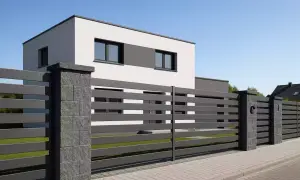 Nowoczesne ogrodzenie z poziomych desek i kamiennych słupków. Idealne, by pokazać, jak zrobić ogrodzenie, które podkreśli styl domu.