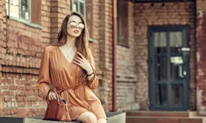 Kobieta w brązowej sukience i okularach przeciwsłonecznych, z torebką. Idealne buty do brązowej sukienki? Zobacz stylizację!
