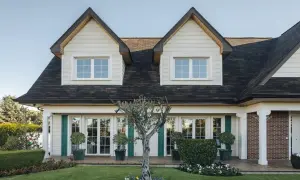 Fachada de casas Canexel con ventanas blancas, contraventanas verdes y un jardín cuidado con un olivo.