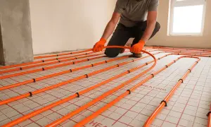 Instalator układa pomarańczowe rury systemu ogrzewania podłogowego. To kluczowy etap prac, by wybrać odpowiednie panele na ogrzewanie podłogowe.