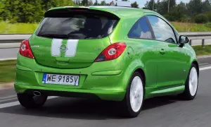 Zielony Opel Corsa D 1.2 benzyna z białymi pasami na klapie bagażnika jedzie po drodze.