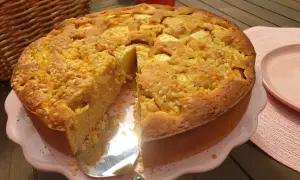 Ein saftiger apfelkuchen ohne zucker, bestreut mit Nüssen, wird auf einem rosa Teller präsentiert. Daneben liegt ein roter Apfel.