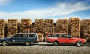 Två Volvo 240 kombi, en blå och en röd, står framför höga staplar av träplankor under en blå himmel.