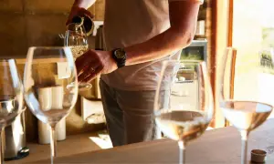 Mężczyzna nalewa białe wino do kieliszka. W tle stoją kolejne kieliszki, sugerując degustację. Wino ma lekko złoty kolor, zapowiadając przyjemny, **medium sweet** smak.