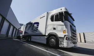 Un camion blanc Scania 770S avec une remorque, garé devant un bâtiment industriel sous un ciel bleu clair.