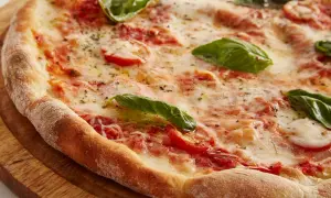 Zbliżenie na świeżo upieczoną pizzę z pomidorami, mozzarellą i bazylią na drewnianej desce.