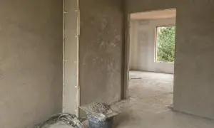 Ściany w trakcie prac wykończeniowych, widoczne tynki cementowo wapienne, wiadro z zaprawą i narzędzia.