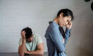 Pareja con intermitencia emocional, ella con la mano en la frente, él con la cabeza entre las manos, ambos de espaldas.