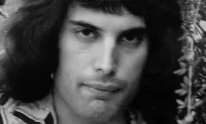Zbliżenie na twarz młodego Freddiego Mercury'ego, którego prawdziwe imię to Farrokh Bulsara. Jego charakterystyczna fryzura i spojrzenie.