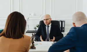 Prawnik wyjaśnia parze, jak napisać wniosek o rozwód. Na stole widać figurkę Temidy.