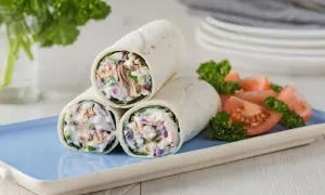 Trois wraps au thon crémeux, garnis de thon, oignons rouges et concombre, servis avec des quartiers de tomates et du persil.