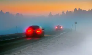Dwa samochody jadące we mgle, ich czerwone światła przeciwmgielne tylne rozświetlają drogę o wschodzie słońca.
