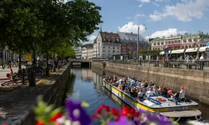 En paddanbåt med turister glider fram på kanalen i Göteborg. Blommor i förgrunden ger en färgklick.