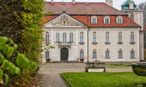 Pałac w Nieborowie z czerwoną, ceramiczną dachówką i ozdobnym frontonem. Wokół jesienne liście i bujna zieleń.