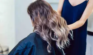 Kobieta z pięknym balejażem blond, jej włosy falują w świetle salonu.