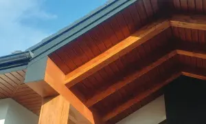 Drewniane belki i boazeria tworzą piękny wykończenie dachu, kontrastując z ciemnym rynną i błękitem nieba.