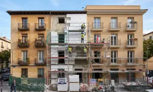 Trabajadores en andamios renuevan fachadas de edificios, aplicando aislamiento térmico. Se ve un cartel de "OBRA SATE".