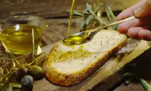 Olio d'oliva versato su pane, con olive e rametti d'ulivo. Un assaggio dei sapori autentici degli oleifici puglia.