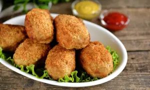 Six croquettes de crevette dorées et croustillantes sur un lit de laitue, avec des sauces moutarde et ketchup en arrière-plan.