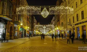 Toruń stare miasto nocą, udekorowane świątecznymi lampkami. Brukowana ulica pełna ludzi, otoczona kamienicami.