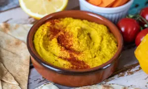 En skål med krämig hummus, toppad med paprikapulver, serveras med pitabröd, citron och grönsaker. Perfekt för ett enkelt hummus recept.