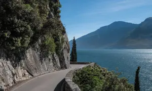 Strada panoramica lungo il lago, con rocce a sinistra e montagne sullo sfondo. La gardesana occidentale offre scorci mozzafiato.