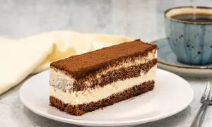 Pyszne ciasto czekoladowe z mascarpone, posypane kakao, na białym talerzu, obok filiżanka kawy.