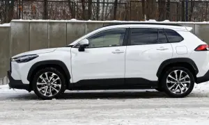 Biała Toyota Corolla Cross Hybrid na tle betonowego muru i śniegu. Stylowy SUV gotowy na zimowe wyzwania.