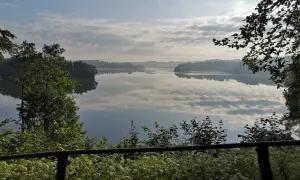 Spokojny poranek nad jeziorem w Sulęczynie. Lustrzana tafla wody odbija chmury i zalesione brzegi.