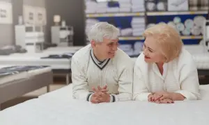 Starsza para rozmawia, leżąc na białym materacu w sklepie.