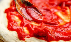 Ein Löffel verteilt die leuchtend rote San Marzano Pizza Sauce auf einem frischen Pizzateig.