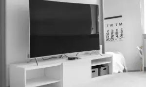 Nowoczesny salon z dużym telewizorem, którego wymiary to 75 cali, na białej szafce RTV. Obok lustro z kalendarzem.