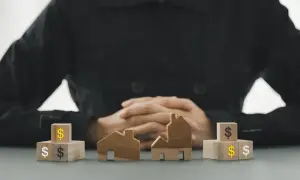 Drewniane domki i kostki z symbolami dolara sugerują **przepisanie mieszkania w formie darowizny**.