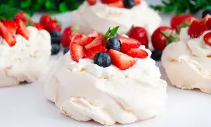 Mini bezy pavlova z bitą śmietaną, truskawkami i borówkami. Pyszny deser na letnie popołudnie.