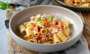 En skål med rigatoni pasta med salsicciapasta recept, toppad med riven parmesan och färsk basilika.