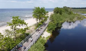 Ludzie na rowerach przemierzają malowniczą trasę Velo Baltica wzdłuż plaży i spokojnej wody.