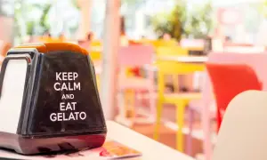 Na stoliku stoi czarny dozownik na serwetki z napisem "Keep calm and eat gelato". W tle kolorowe krzesła w kawiarni. To dobre hasło na lato!
