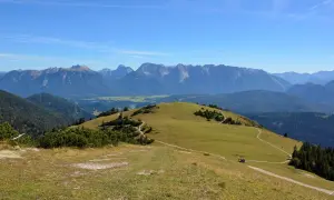 Ein sonniger Tag lädt zum **Wank wandern** ein. Grüne Hügel mit verschlungenen Pfaden erstrecken sich vor einer majestätischen Bergkulisse.