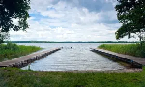Dwa drewniane pomosty prowadzące na spokojne jezioro, otoczone zielenią. Idealne miejsce na relaks i podziwianie przyrody, jedna z wielu atrakcji w Boszkowie.