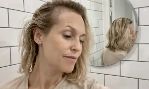 Kvinna med blont hår tittar ner, reflekteras i spegeln. Hon verkar orolig över att tappa hår under amning.