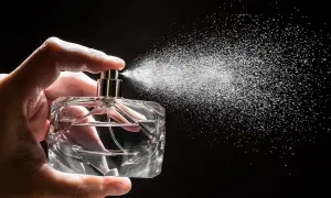 Dłoń trzyma szklaną buteleczkę, z której rozpyla się mgiełka. To woda perfumowana, a nie perfumy, tworząca subtelny zapach.