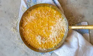En gyllene risotto milanese, toppad med riven parmesan, i en metallpanna på en marmorskiva.