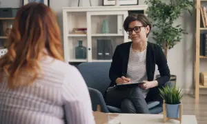 Psychoterapeutka w okularach notuje coś na kartce podczas rozmowy z pacjentką w gabinecie.