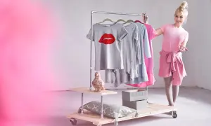 Stylowy wieszak na kółkach z ubraniami i dekoracjami. Kobieta w różowej sukience prezentuje ubrania.