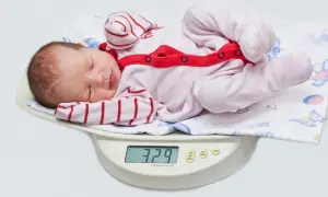 Nowe życie waży 3,29 kg. Dziecko po urodzeniu leży na wadze, ubrane w różowy pajacyk w paski.