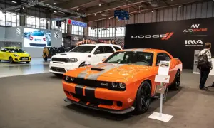 Pomarańczowy Dodge Challenger SRT Hellcat z czarnymi pasami na masce, obok białego Durango i żółtego Suzuki.
