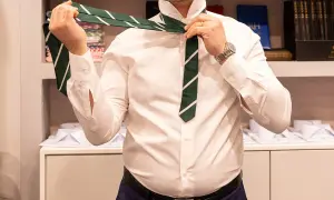 Uomo con camicia bianca che si lega il nodo cravatta inglese verde a righe bianche.