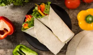 Dwa tortille z warzywami na talerzu, obok papryki i pomidorów. Idealne do szybkiego posiłku, a jak przechowywać tortille? W szczelnym opakowaniu!